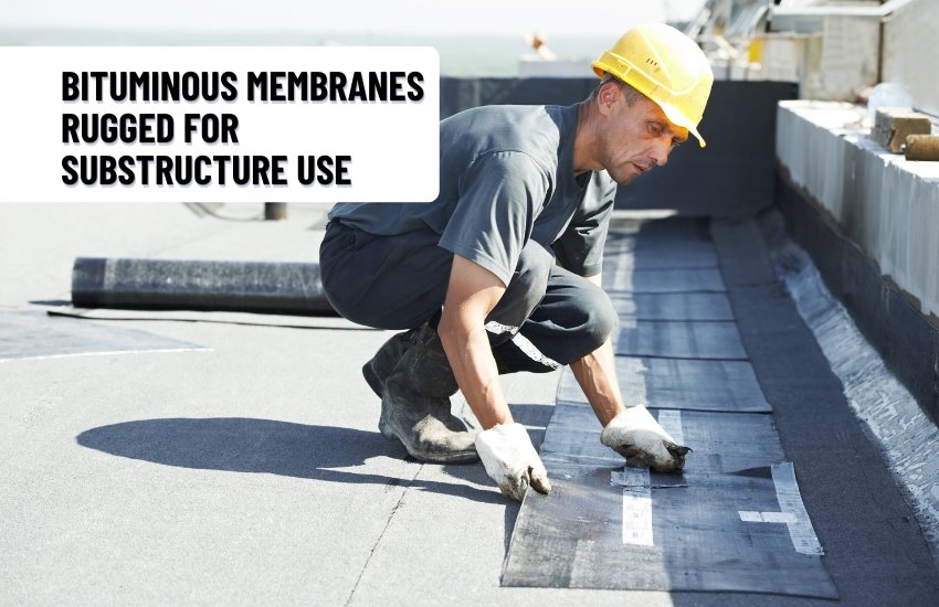 Prashita Associates A construction worker in a yellow hard hat installs a bituminous waterproofing membrane on a flat rooftop. He is kneeling on the surface, aligning the black membrane strips carefully, with rolled material in the background. A white text box reads, “Bituminous Membranes – Rugged for Substructure Use.